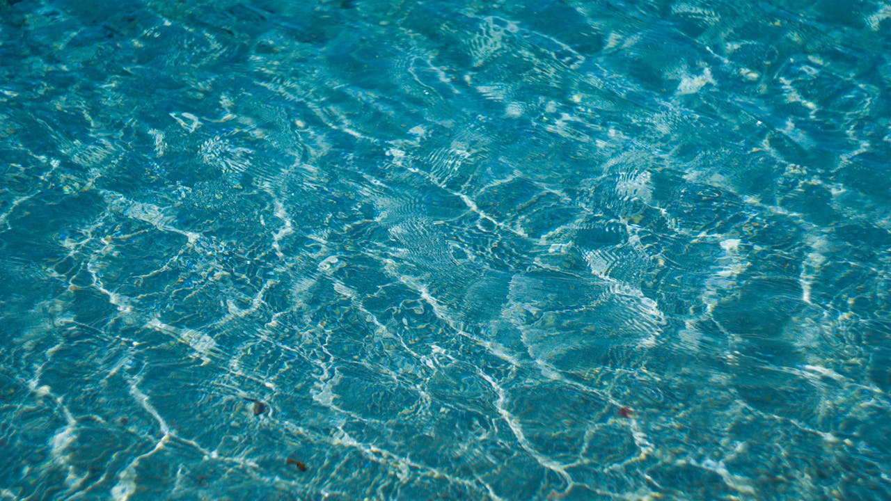 Das Sonnenlicht spiegelt sich auf der Oberfläche des klaren blauen Wassers und erzeugt wellenförmige Muster und Wellen - ähnlich wie das glatte Ergebnis einer erfolgreichen Fettabsaugung. Das Wasser erscheint hell und einladend, mit verschiedenen Blautönen und schimmernden Highlights.