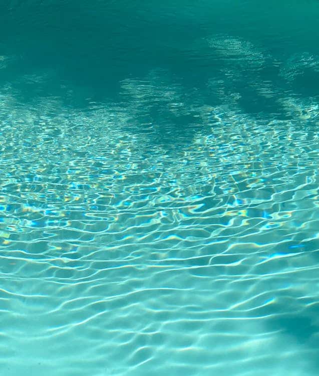 Das Sonnenlicht spiegelt sich auf der klaren, türkisfarbenen Oberfläche des ruhigen Wassers und erzeugt kräuselnde Muster und schimmerndes Licht auf dem Boden des Pools, was an die sanfte Ausstrahlung erinnert, die oft bei Faltenbehandlungen angestrebt wird.